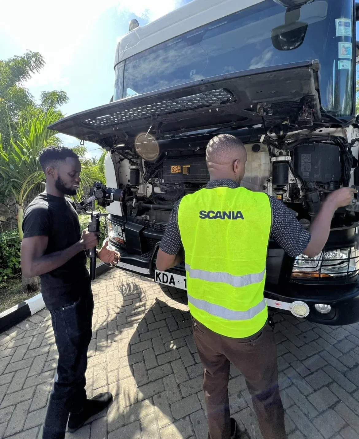 A camera operator with a gimbal films a Scania technician working on a truck engine