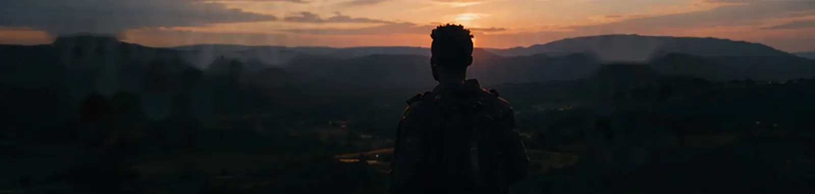 A figure standing before hills at sunset