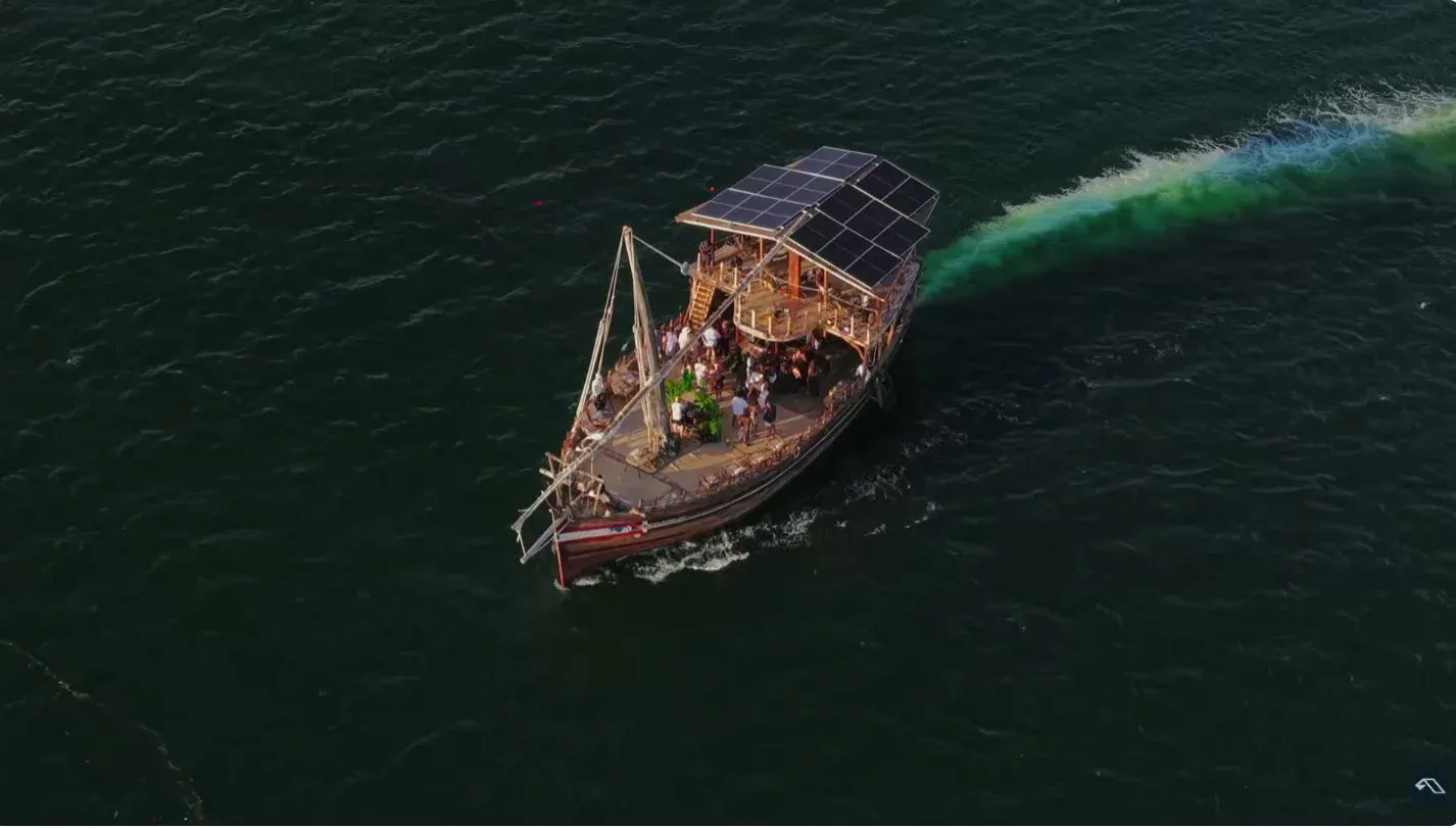 Aerial view of a dhow with people on deck crossing dark green water